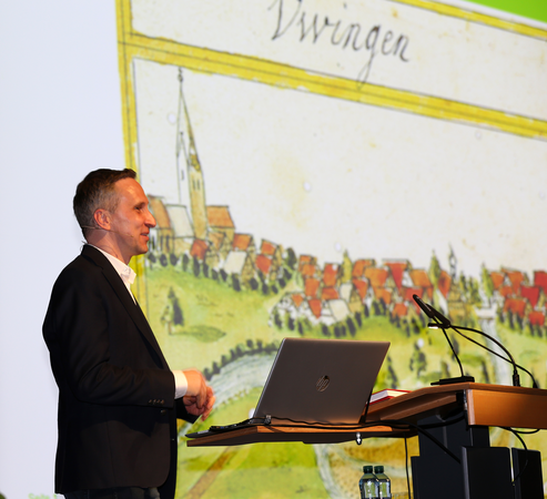 Kreisarchivar Dr. Steffen Lang steht an einem Rednerpult und hält eine Präsentation vor einer historischen Karte mit einem Laptop darauf.