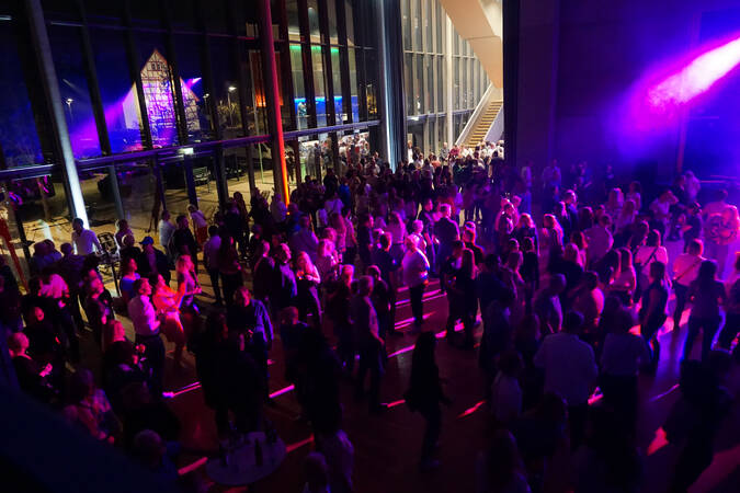 Viele Menschen tanzen in einem großen, mit buntem Licht beleuchteten Saal.