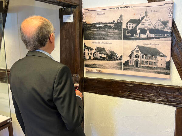 Ein Mann im Anzug betrachtet ein historisches Fotoposter mit vier verschiedenen Ansichten von Gebäuden aus Uhingen.