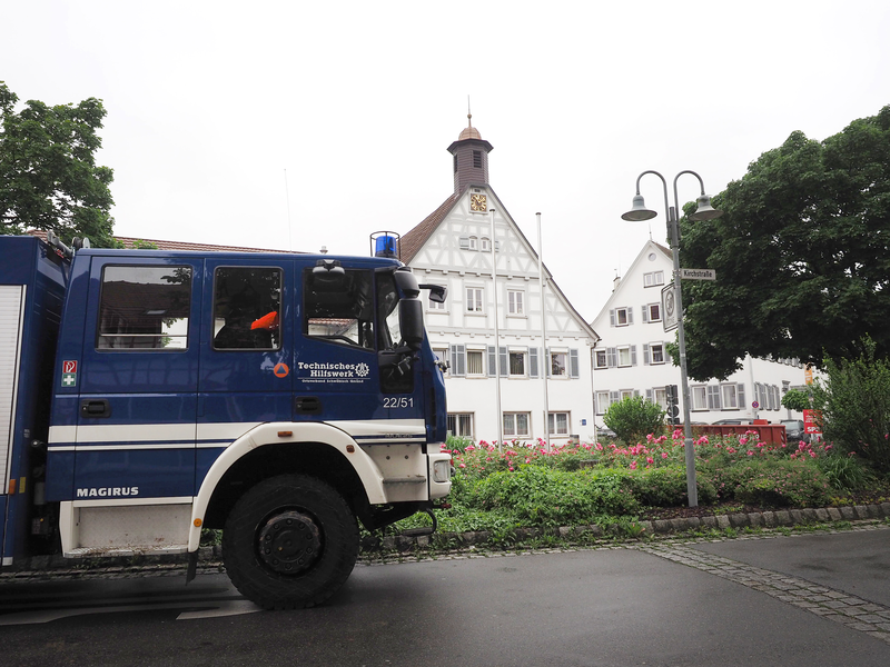 Ein blaues Einsatzfahrzeug des Technischen Hilfswerks steht vor einem historischen Fachwerkgebäude mit Turmuhr, umgeben von Blumenbeeten und Bäumen.