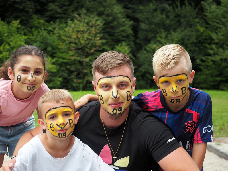 Ein Betreuer und drei Kinder haben sich das Gesicht schminken lassen: ein gelber Kreis mit dem Schriftzug "BVB 09" für den Fußballverein Borussia Dortmund.