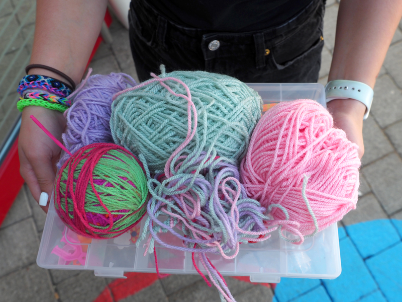 Eine Betreuerin trägt eine Plastikschale, auf der mehrere große und dicke Wollknäule unterschiedlicher Farbe liegen.