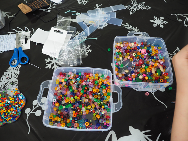 In durchsichtigen Plastikkistchen sind kunterbunte Perlen, daneben liegen Scheren und Bindfaden.