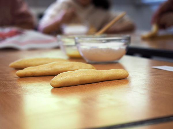 Drei kleine Rollen aus Hefeteig liegen auf einem Tisch, dahinter sind zwei Schüsseln: mit Puderzucker und Eigelb.