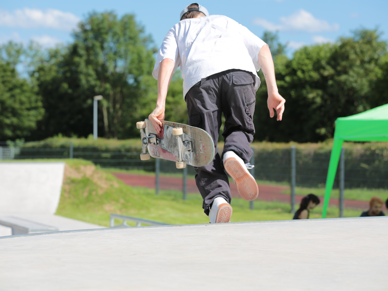 Ein Skater von hinten, der in der linken Hand ein Skateboard hält und eine Rampe hinunterrennt, um mit dem Skateboard zu fahren.