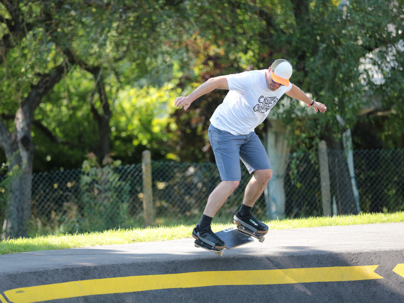 Ein Mann steht in kurzen Hosen auf einem Skateboard an einer Rampe aus grauem Beton und will hinabfahren. 