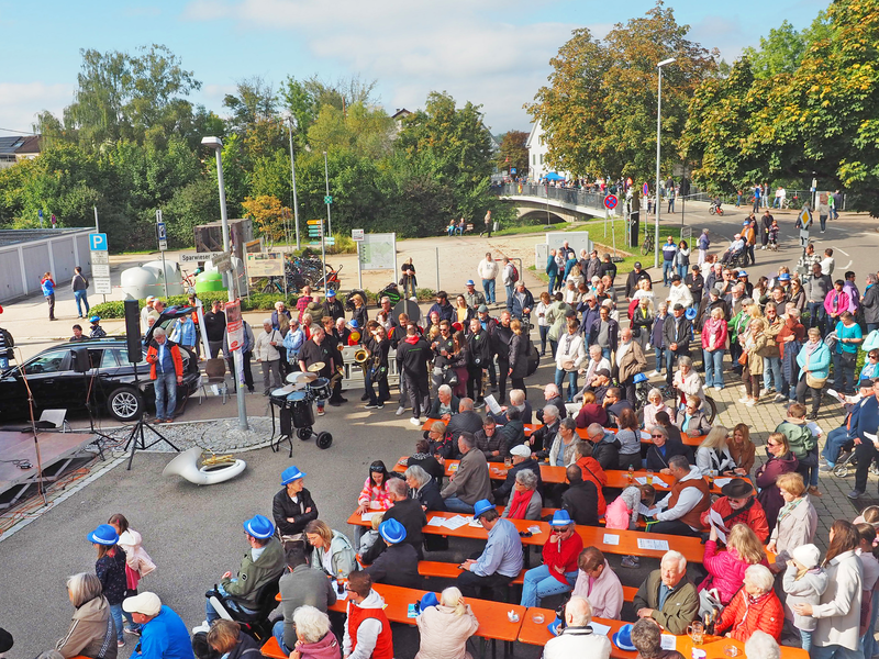Eine große Menschenmenge mit Musikern versammelt sich bei sonnigem Wetter um Tische und Bänke rund um das Uhinger Rathaus zum Fest der Musik.