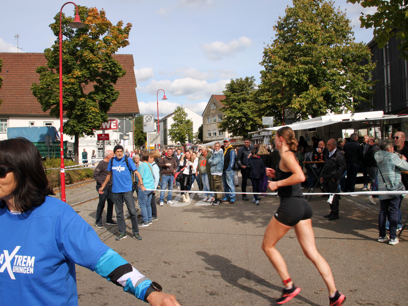 Eine Frau läuft im Sport-Outfit über eine gesperrte Straße an Passanten vorbei, die entlang von Geschäften flanieren.