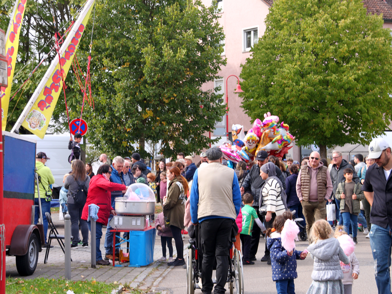 Menschen flanieren auf einer abgesperrten Straße beim verkaufsoffenen Sonntag, an einem Stand sind bunte Heliumballons.