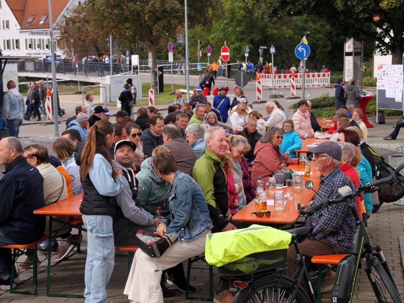 Menschen sitzen an Biertischgarnituren und trinken gemütlich und essen etwas.