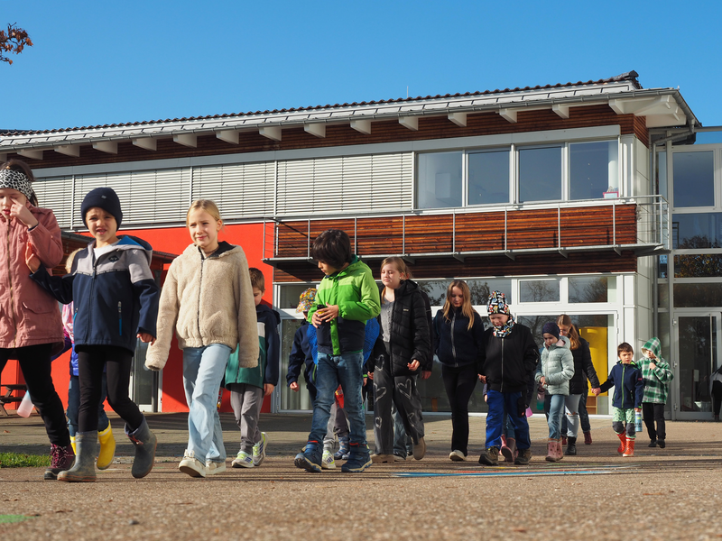Eine Gruppe von Kindern in bunter Kleidung geht gemeinsam über den Schulhof der Grundschule in Sparwiesen.