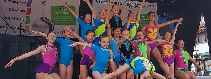 Kinder in bunten Gymnastikanzügen posieren mit gestreckten Armen auf einer Bühne