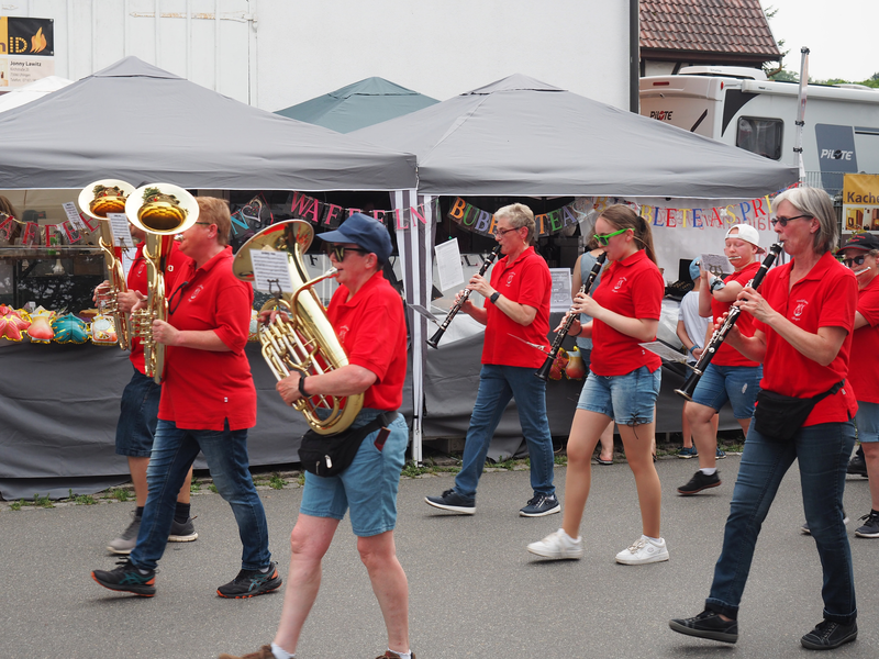 Musiker marschieren, ihre Instrumente spielend, an Festständen auf einer Straße vorbei.