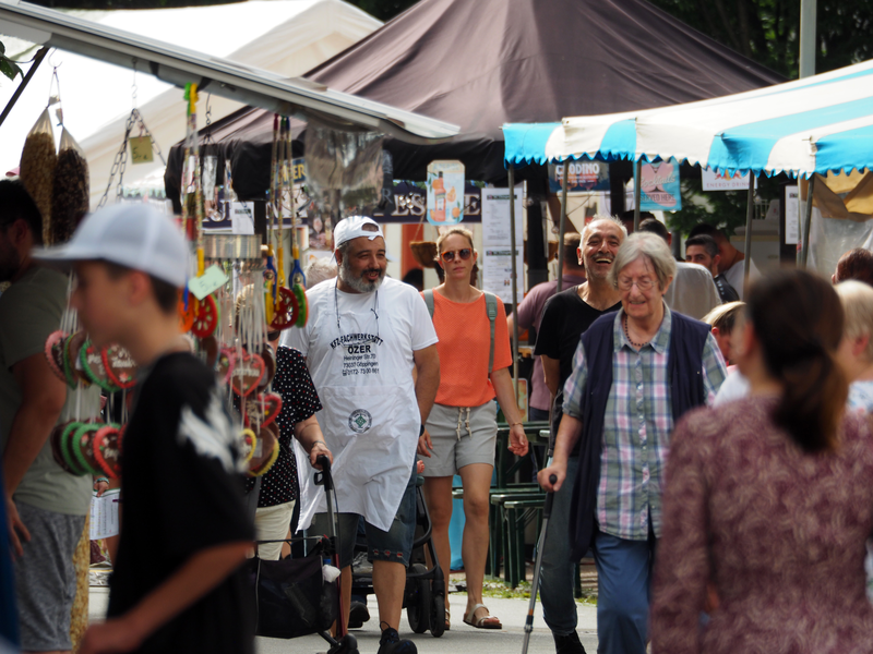 Menschen flanieren entlang von Festständen über eine Straße.