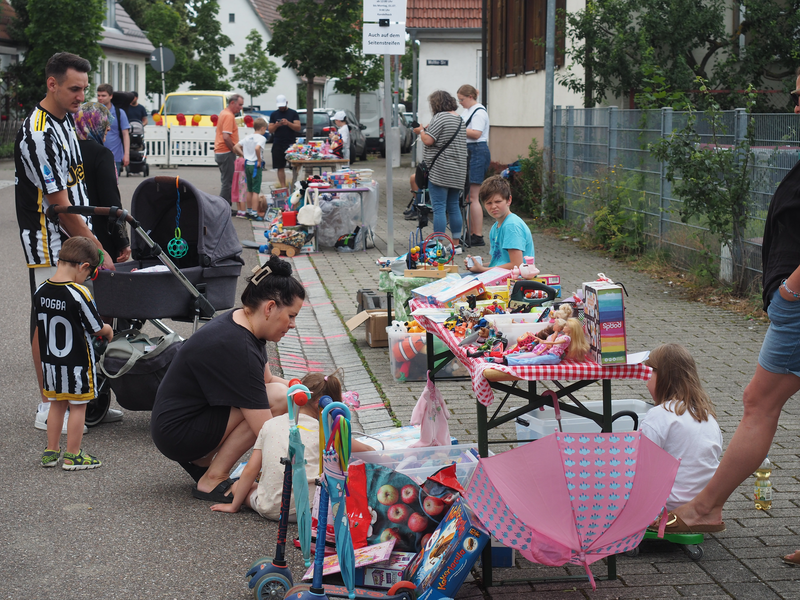 Passanten vor einem Stand beim Kinderflohmarkt, auf einem Tisch stehen Spielsachen.