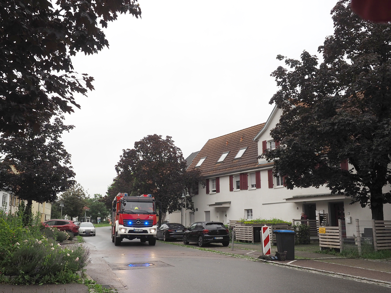 Ein Feuerwehrfahrzeug fährt mit Blaulicht auf einer Straße an Häusern vorbei.