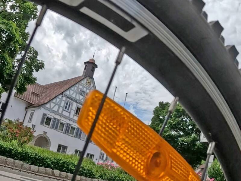 Ein altes Fachwerkgebäude mit einem Turm - das Rathaus in Uhingen - ist durch die Speichen eines Fahrrads mit einem orangenen Reflektor sichtbar.